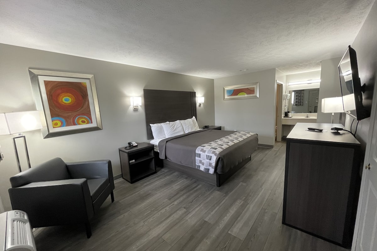 A hotel room with a bed, bedside tables, a desk, a chair, a TV, and artwork on the walls.