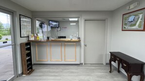 A reception area with a counter, a television mounted on the wall, a door, and a window with a view of a parking lot. - Embassy Inn (Hohenwald)
