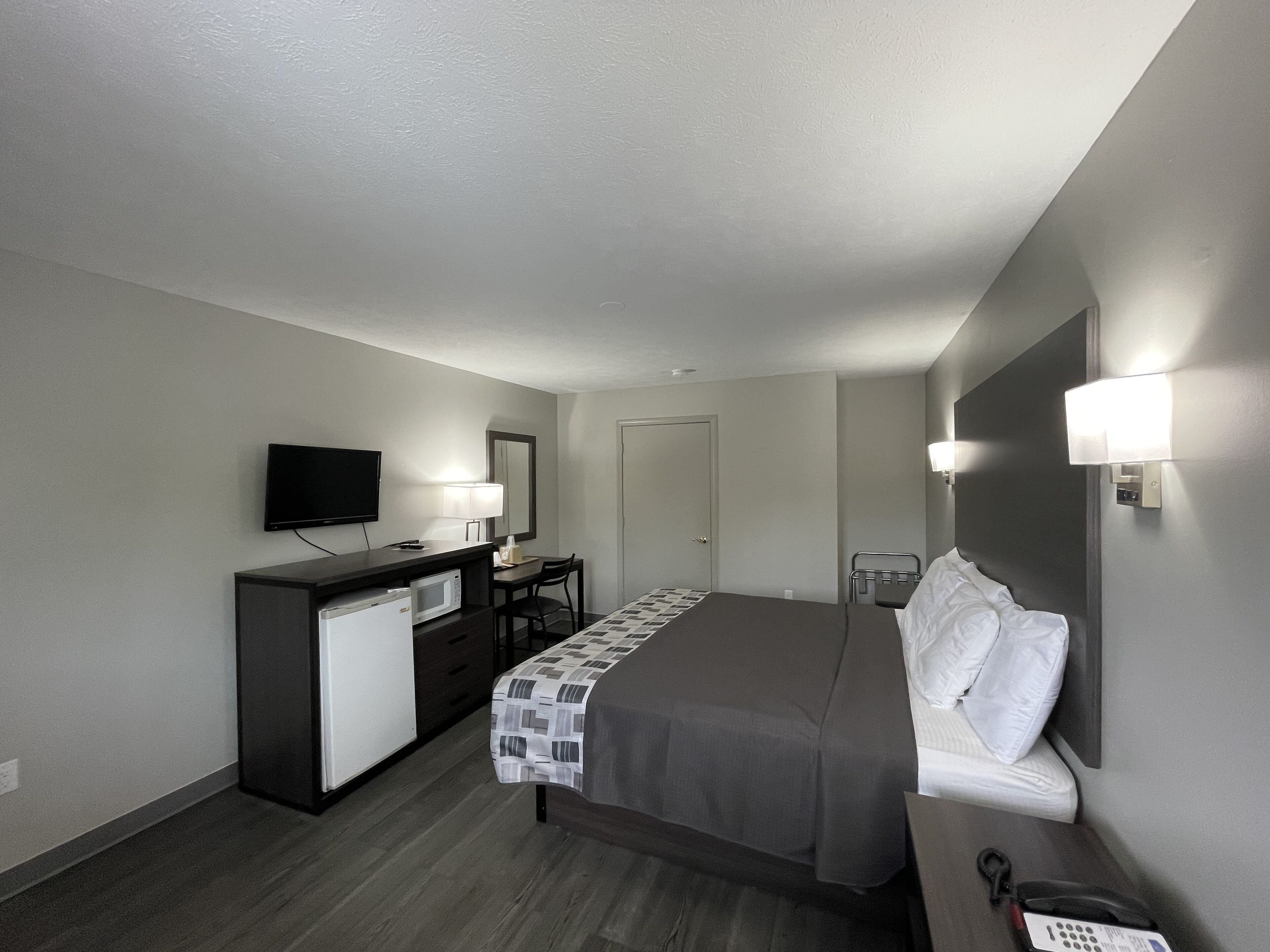 Una habitación de hotel con una cama, un escritorio con televisor, microondas y una silla.