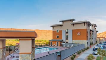 A hotel with a pool, outdoor seating, and a view of the mountains.