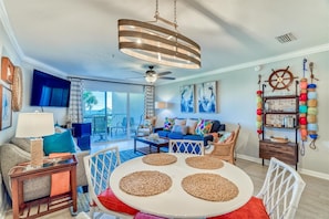 Cozy living room with a round table, comfortable seating area, and a large window offering a view of the outdoors.