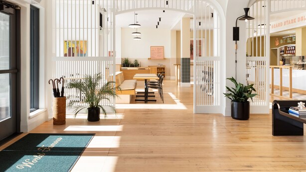 A spacious hotel lobby with wooden flooring, a reception desk, and a staircase leading to upper floors.