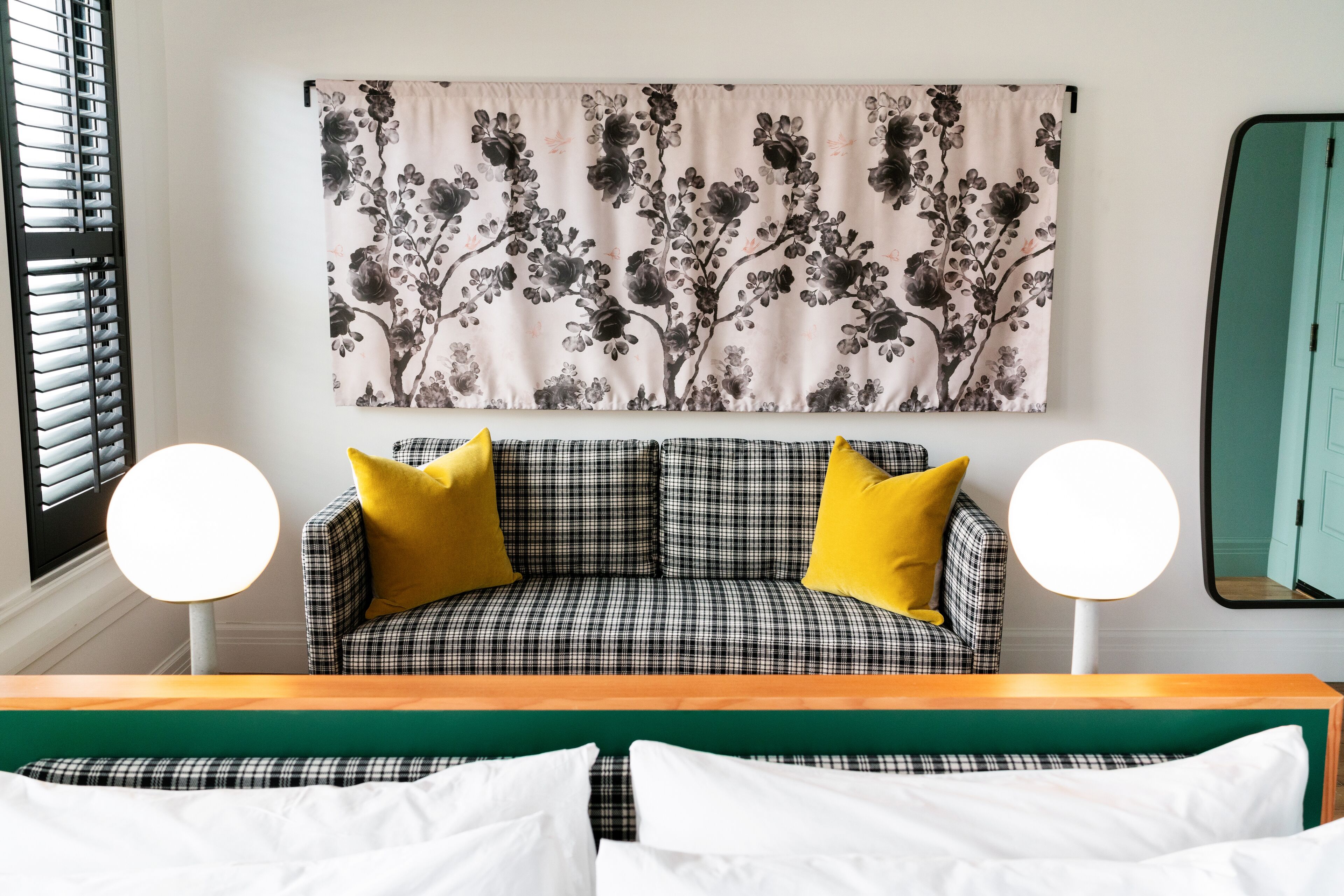 A room with a checkered sofa, two yellow pillows, a green headboard, and a floral tapestry on the wall.
