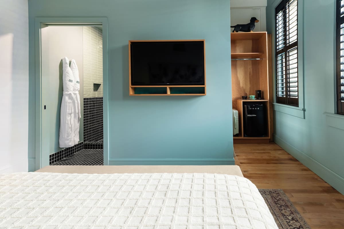 A bedroom with a bed, a TV mounted on the wall, a wooden wardrobe, and a window with shutters.