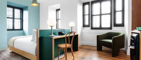Un dormitorio con cama, escritorio, silla y ventanas grandes.