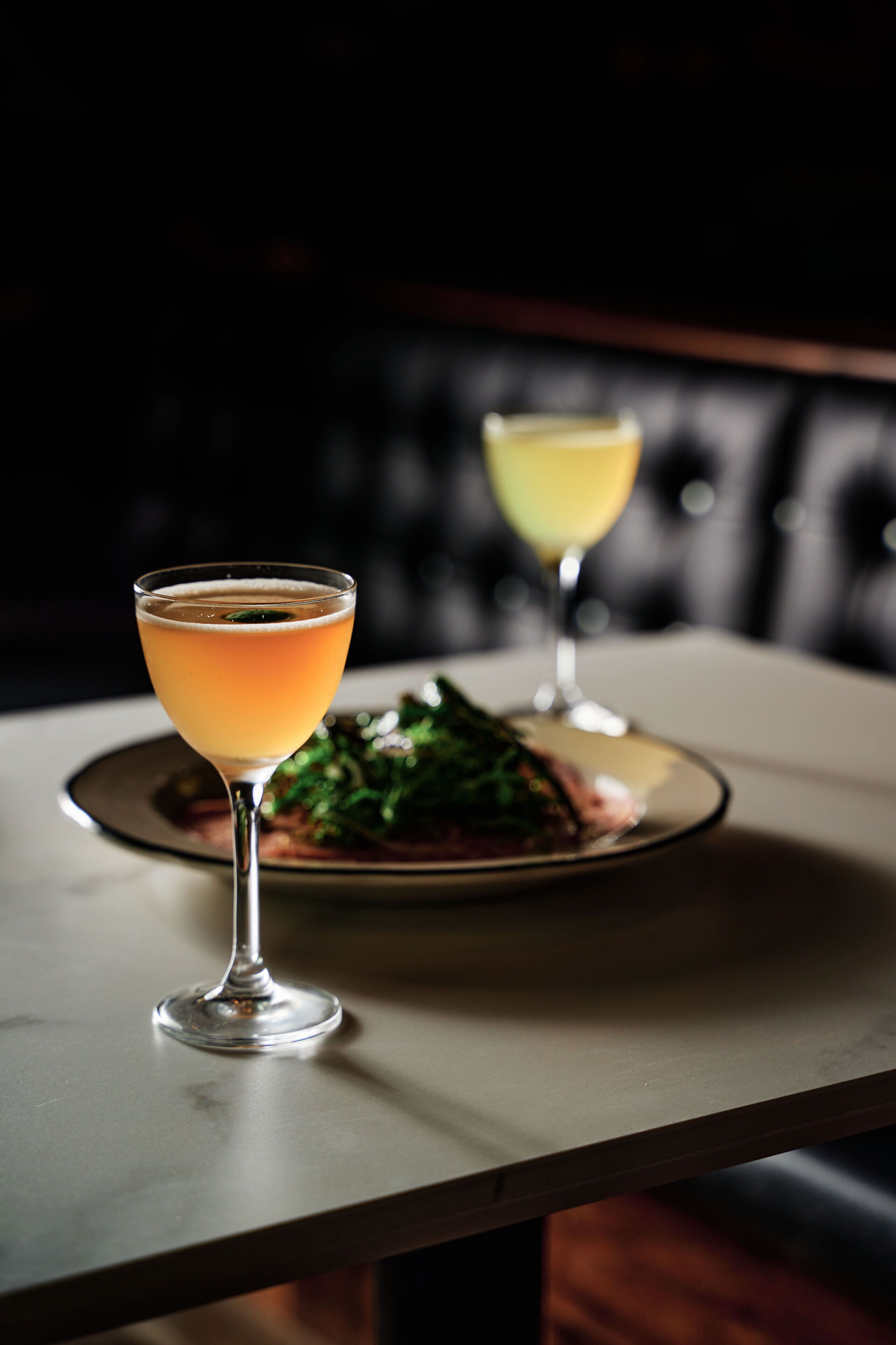 A table with two glasses of cocktails and a plate of food.
