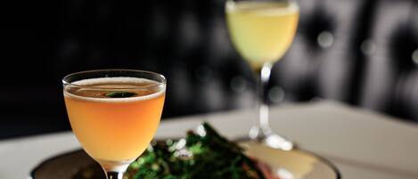A table with two glasses of cocktails and a plate of food.