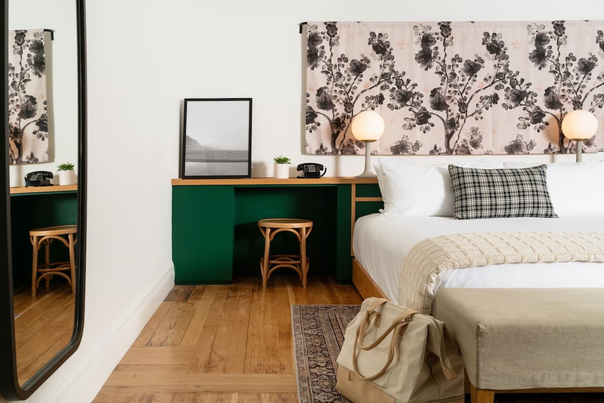 A bedroom with a bed, a desk, two lamps, a mirror, and a floral headboard.