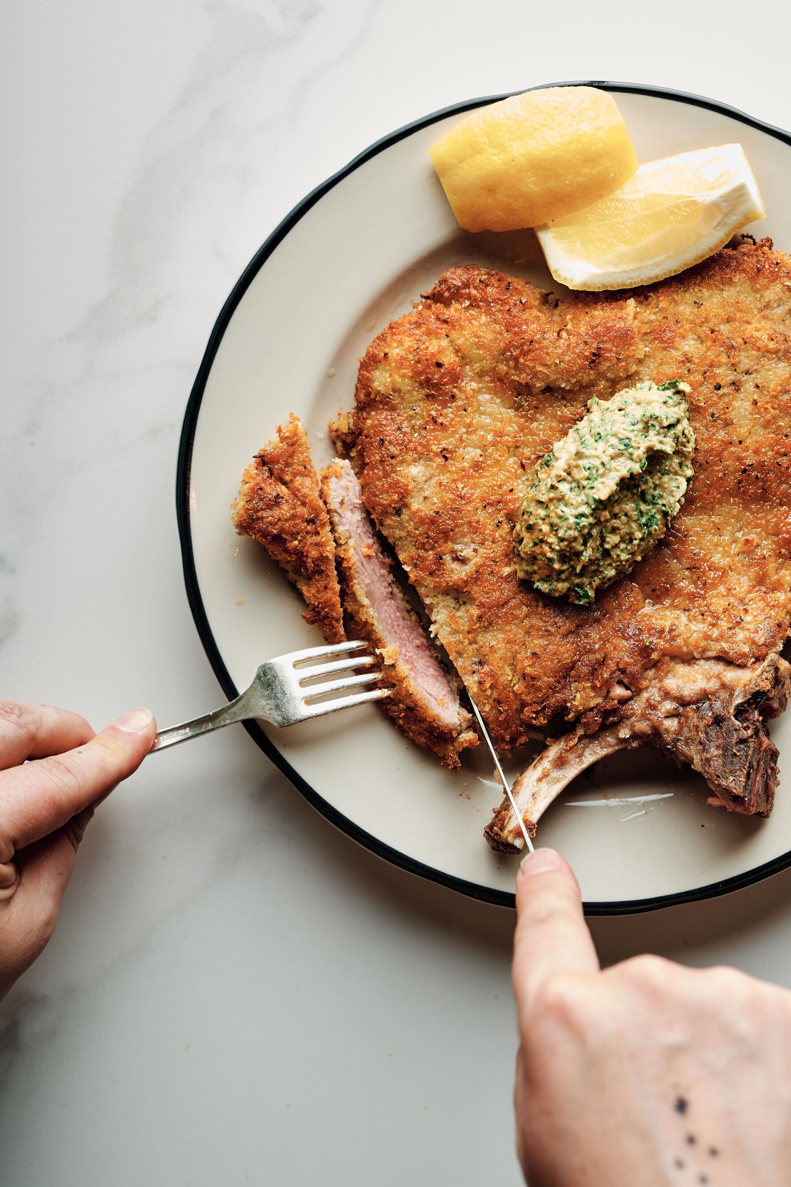 A plate with a breaded meat cutlet, lemon wedges, and a dollop of sauce.