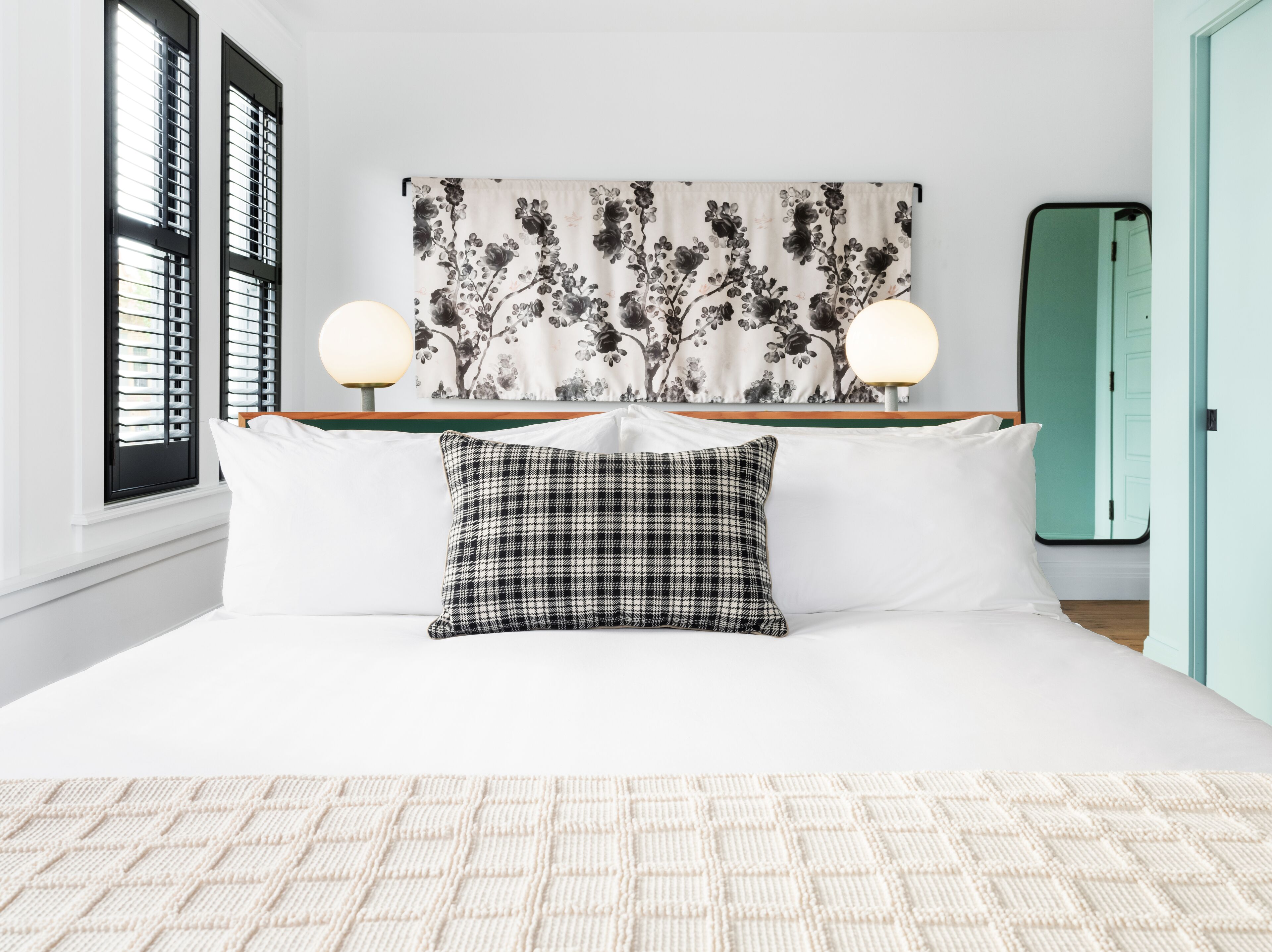 Un dormitorio ordenado con una cama, dos lámparas de noche, un cabecero estampado con motivos florales y una almohada de cuadros.