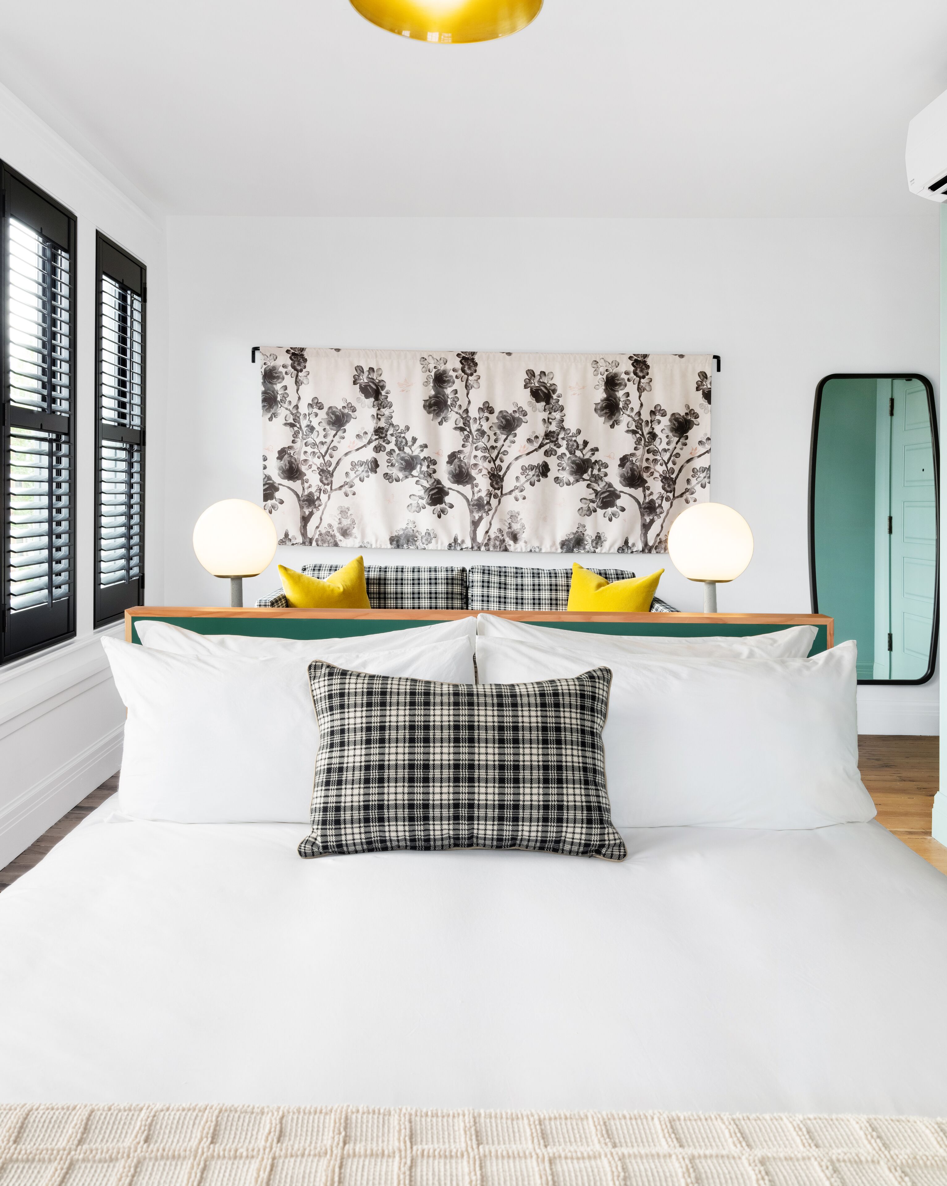 Une chambre à coucher moderne avec un lit, deux lampes de chevet, une tapisserie à motifs floraux et une porte verte.