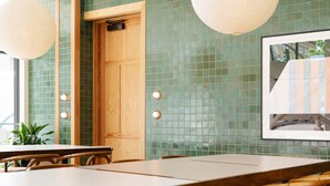A dining area with a wooden table and chairs, green tiled walls, and hanging paper lanterns.