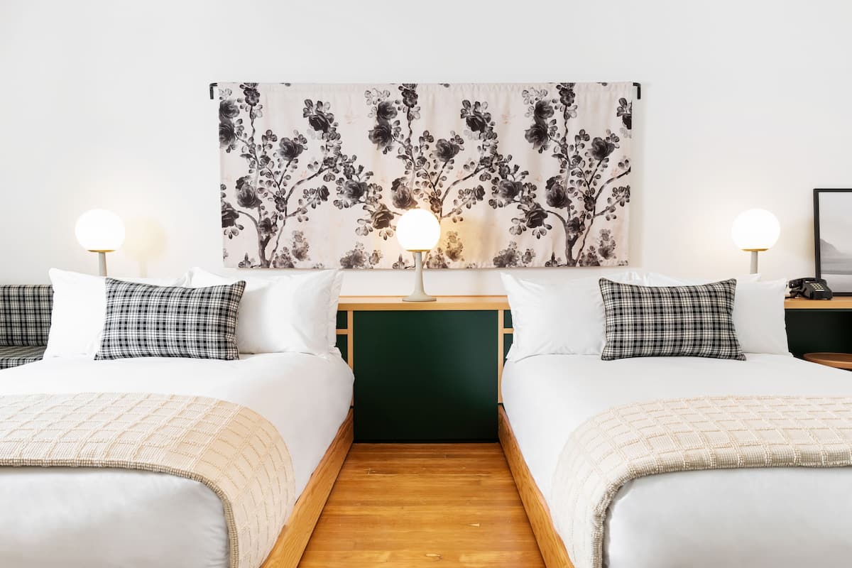 A hotel room with two beds, a floral artwork above the beds, and bedside lamps.