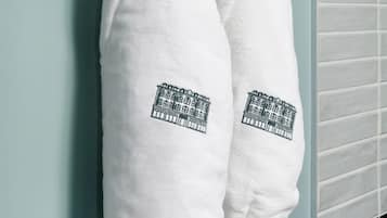 Two white towels with a building design hanging on a teal wall.