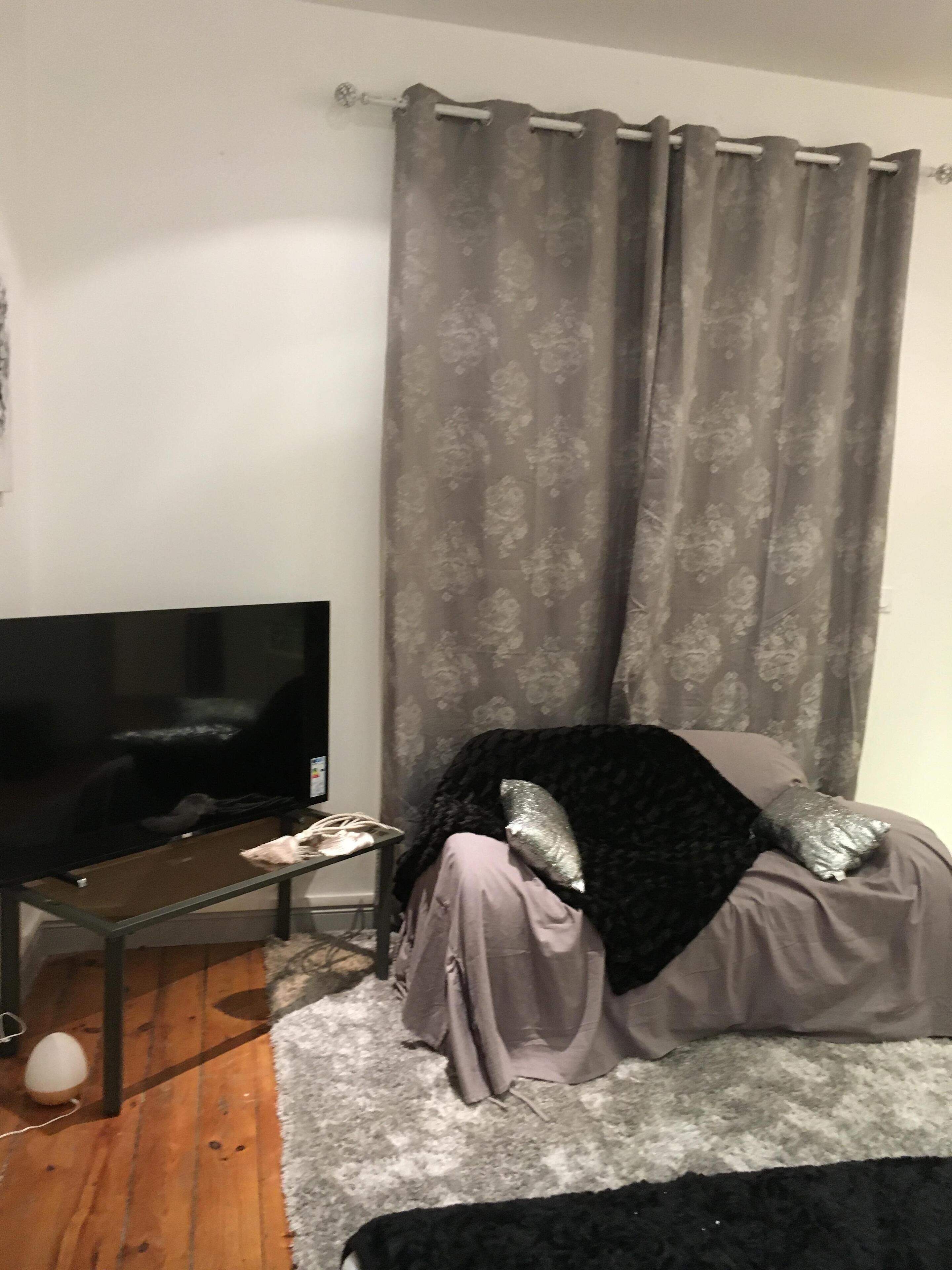 Een slaapkamer met een bed, een tv op een standaard, een grijze gordijn en een muur met een grijs patroon.