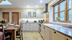 Una cocina moderna con armarios de madera, un comedor con mesa dispuesta para cuatro personas y un ventanal con vistas a árboles.