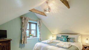 Un dormitorio con cama, televisor, ventana con cortinas, mesita de noche con lámpara y luz de techo.