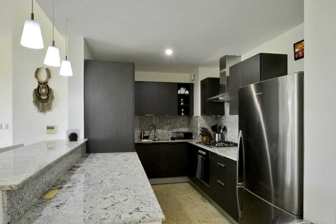 A modern kitchen with dark cabinets, a stainless steel refrigerator, and pendant lights.