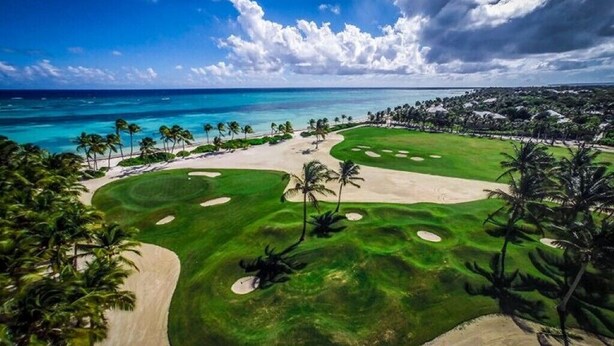 En golfbana med sandbunkrar, palmer och utsikt över havet.