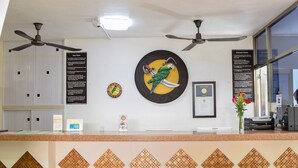 A hotel reception area with a counter, ceiling fans, a clock, a framed certificate, and a decorative wall piece. - 202 Junior Suite w/balcony & living area. (Isla Mujeres)