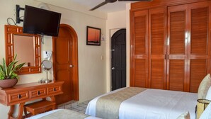 A hotel room with two beds, a TV mounted on a wooden dresser, a potted plant, and a door with a black shutter. - 202 Junior Suite w/balcony & living area. (Isla Mujeres)
