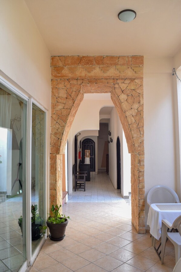 Un pasillo con un arco de piedra, una puerta de cristal, una planta en maceta y una mesa con sillas.