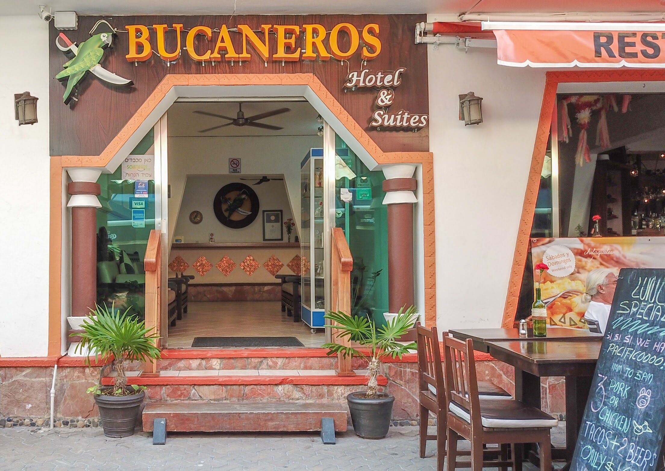 Het uiterlijk van Hotel Bucaneros & Suites, met een bord, ingang en een terras.