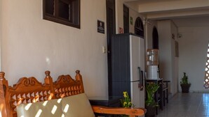 A wooden sofa with a beige cushion in a hallway with tiled flooring, a refrigerator, and a water dispenser. - 202 Junior Suite w/balcony & living area. (Isla Mujeres)