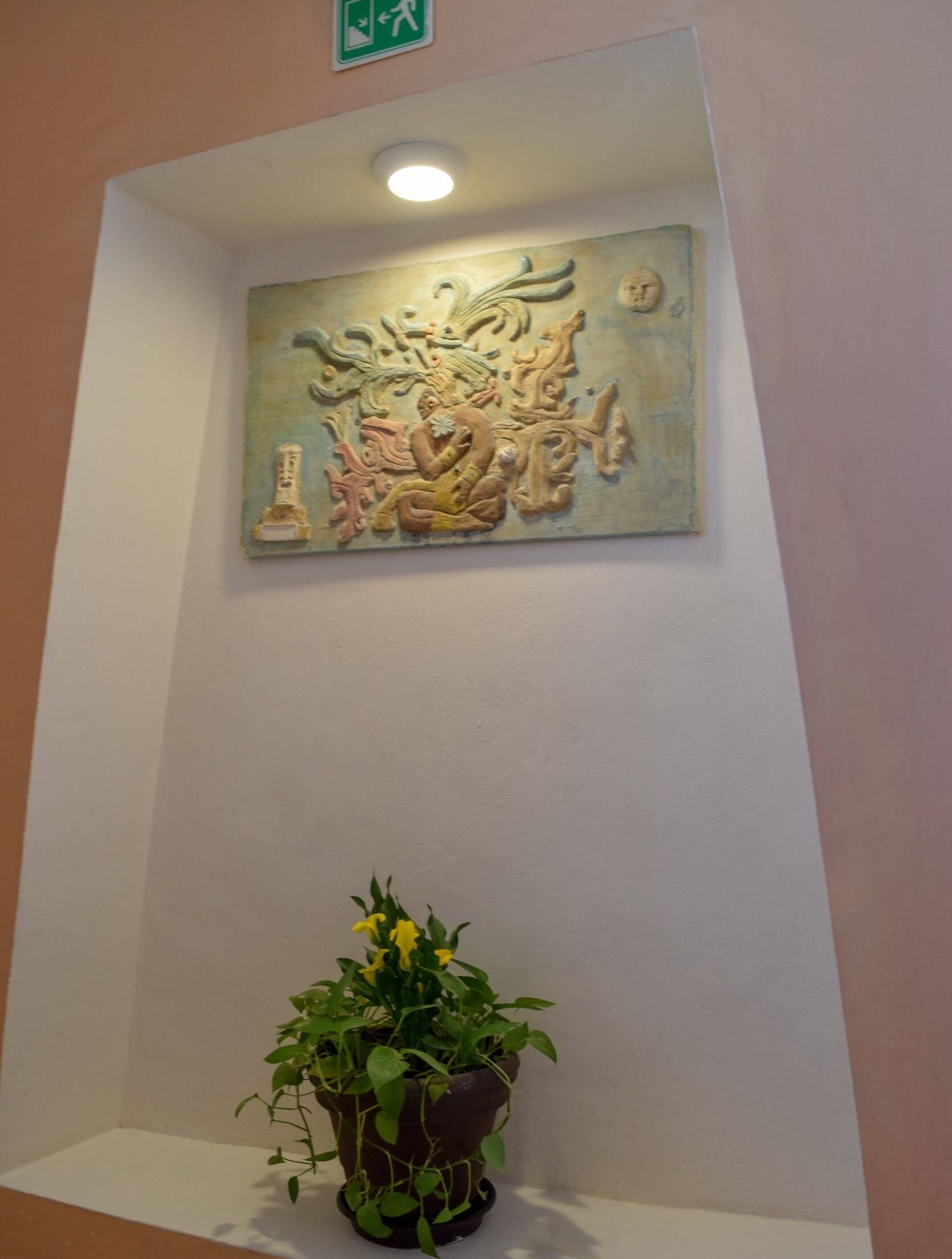 A wall with a textured artwork and a potted plant.