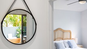 A bedroom with a bed, a wooden headboard, a nightstand, and a mirror on the wall. - Marie’s Byron Escape (Byron Bay)