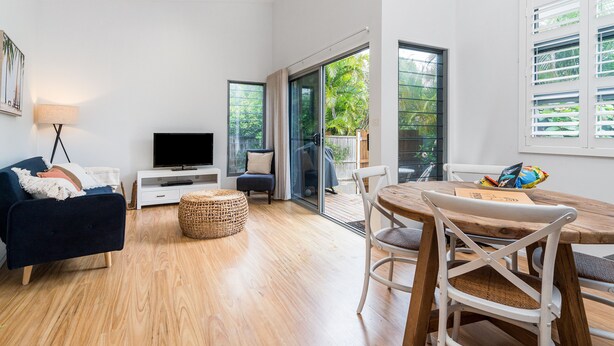 A modern living room with a sofa, TV, and dining area. - Marie’s Byron Escape (Byron Bay)