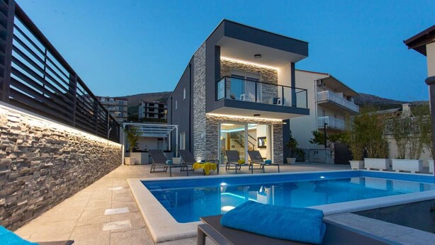 Una casa moderna a due piani con piscina, muro in pietra e zona relax all'aperto.