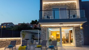 Una casa moderna a due piani con un balcone e una zona salotto esterna.