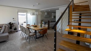 Un soggiorno moderno con zona pranzo, una scala e una cucina sullo sfondo.