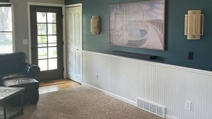 A living room with a dark teal wall, a large painting, a ceiling fan, and a sectional sofa. - Downtown TC Home (Traverse City)