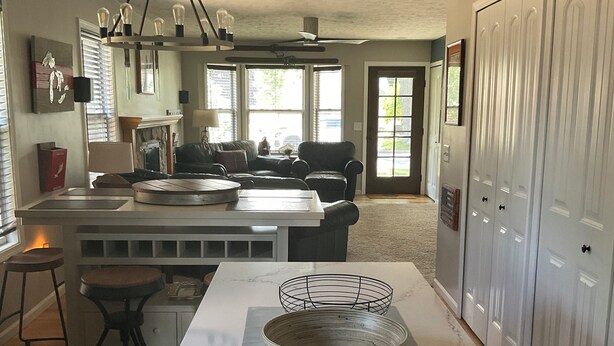A spacious kitchen with a large island, a dining area with a sofa, and a view of the outdoors through large windows. - Downtown TC Home (Traverse City)