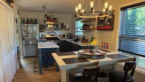 A modern kitchen with a central island, wooden chairs, and a hanging light fixture. - Downtown TC Home (Traverse City)