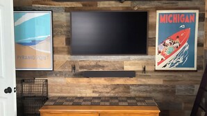 A bedroom with a wooden wall, a flat-screen TV, a dresser, and two posters. - Downtown TC Home (Traverse City)