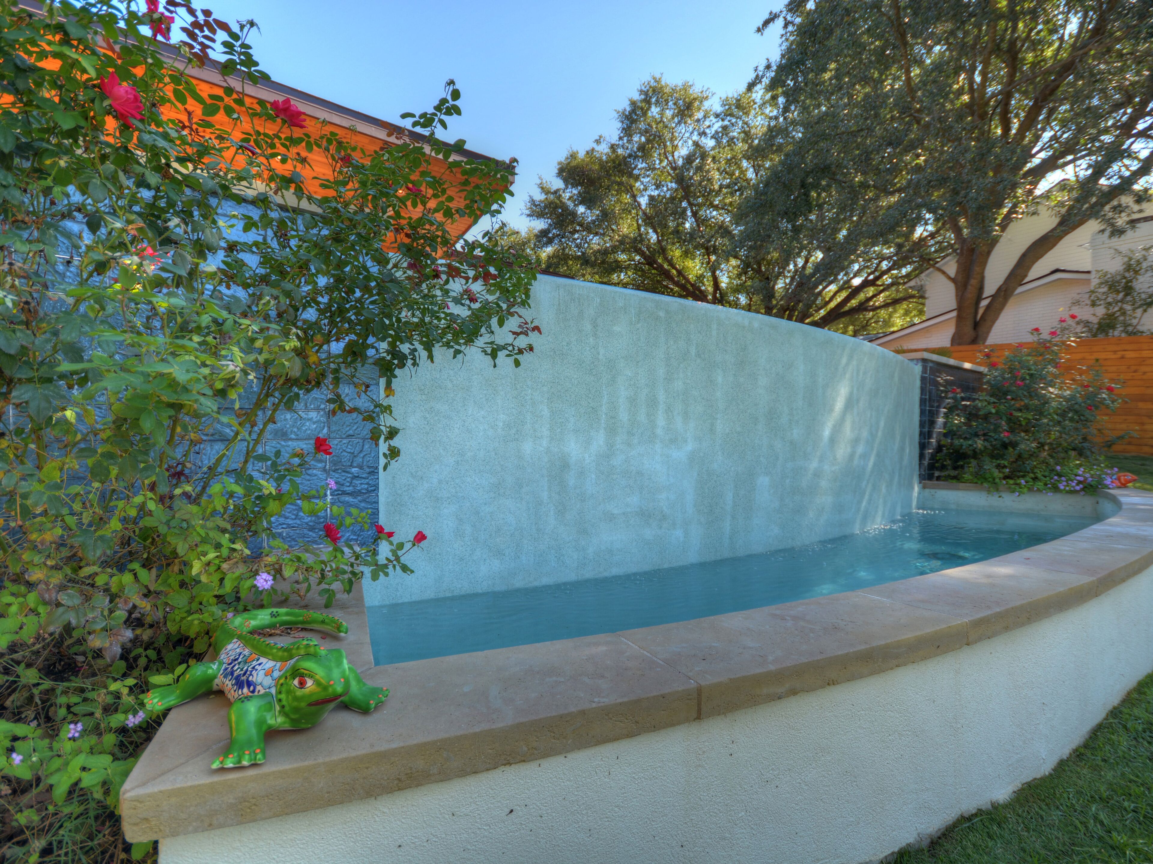 Ein Pool mit Wasserfall, umgeben von Grünpflanzen und einer dekorativen Froschstatue.