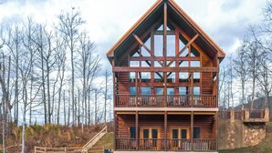 A two-story log cabin with a balcony on the upper floor, surrounded by trees. - Bear's Eye View by Jackson Mountain Rentals (Gatlinburg)