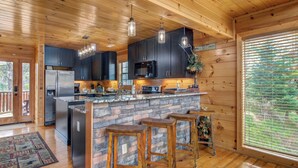 A modern kitchen with dark cabinets, a stone island, and wooden stools. - Bear's Eye View by Jackson Mountain Rentals (Gatlinburg)