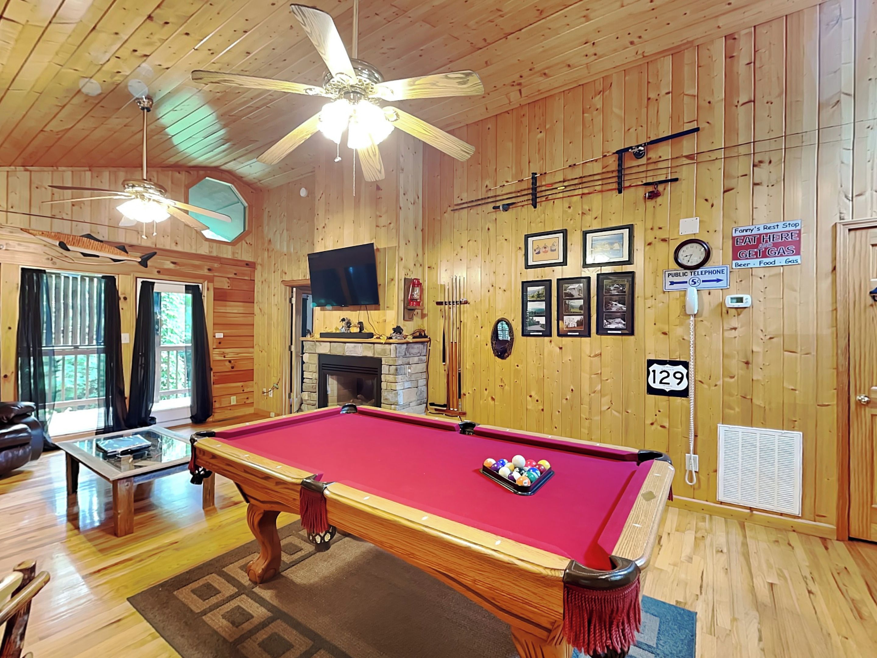 A pool table in a wooden room with a fireplace, ceiling fans, and a sign for a rest stop.