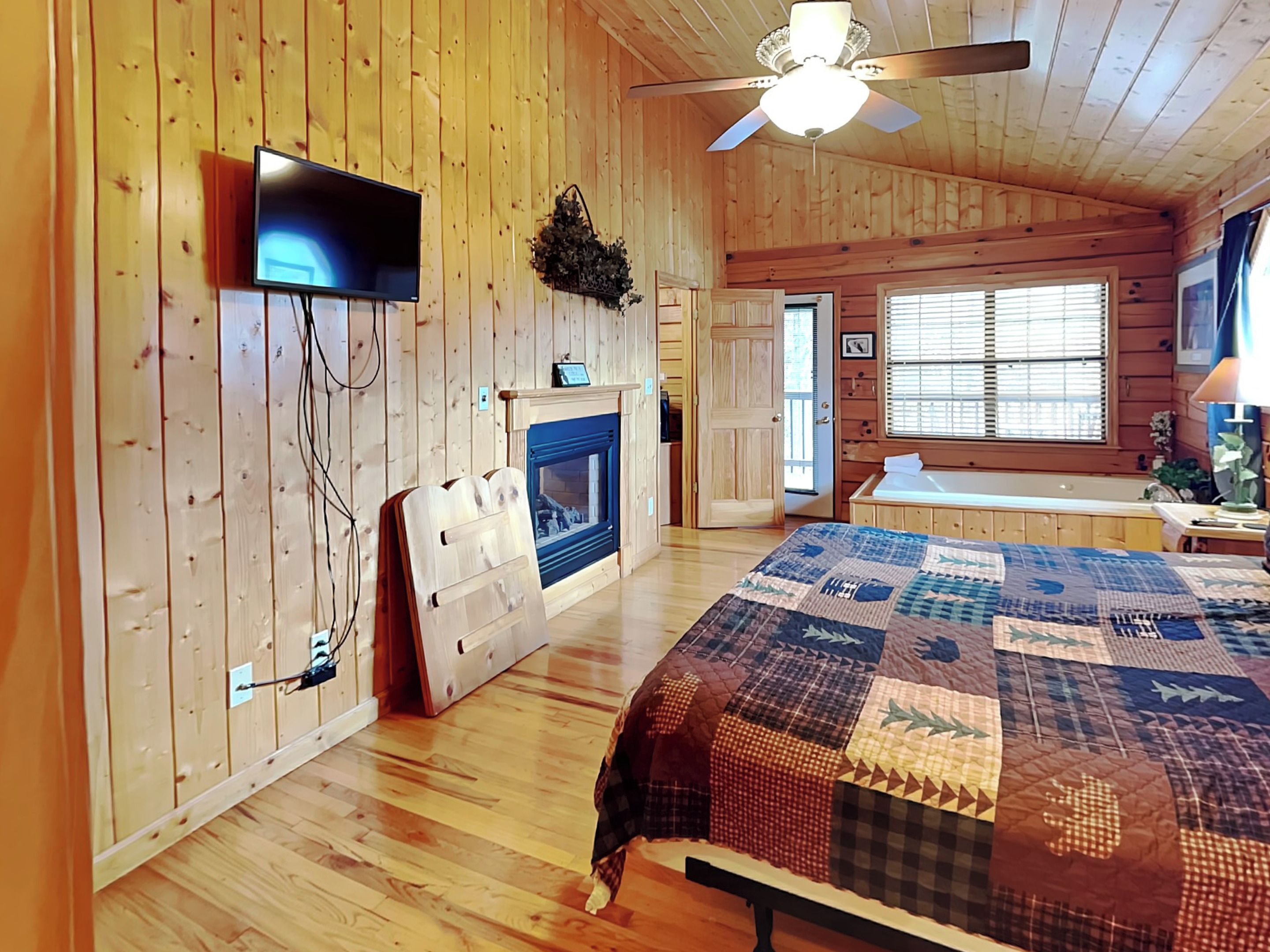 A cozy cabin-style room with a wooden interior, a fireplace, a bed with a quilt, and a ceiling fan.