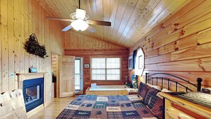 Une chambre confortable dans un chalet en bois, avec un grand lit, une cheminée, un ventilateur de plafond et une fenêtre équipée de stores.