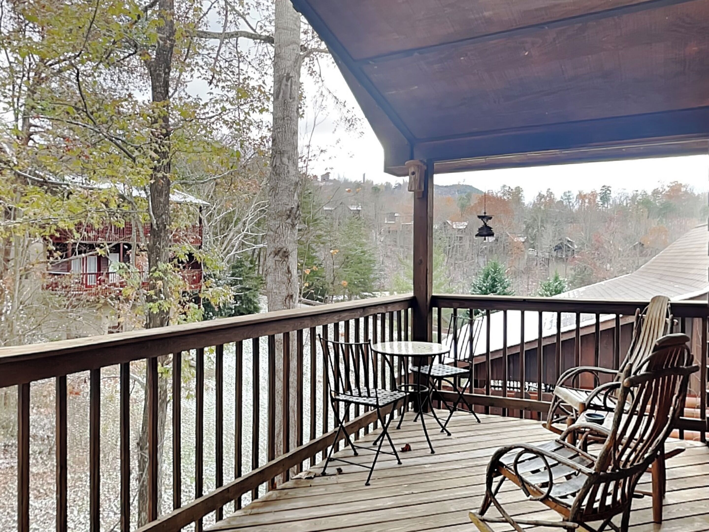 A wooden deck with a railing, a table, and two rocking chairs.
