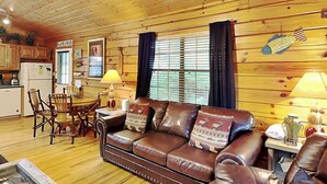 L’intérieur chaleureux d’un chalet avec un canapé en cuir, une table à manger en bois, des chaises et un coin cuisine.