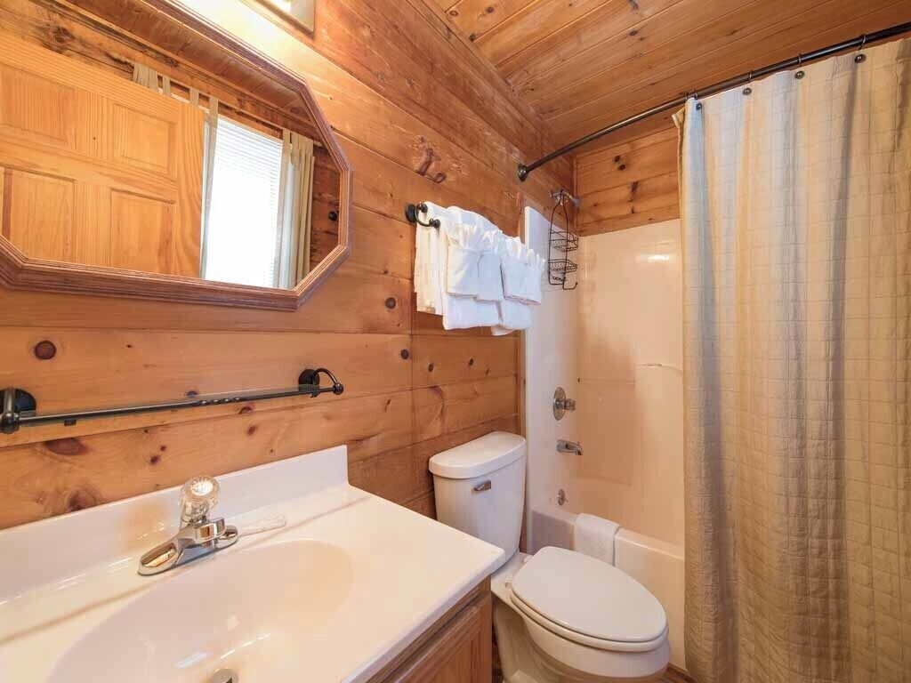 A wooden cabin bathroom with a sink, toilet, and shower.