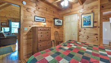 A wooden cabin bedroom with a quilted bedspread, wooden walls, a ceiling fan, and a dresser.