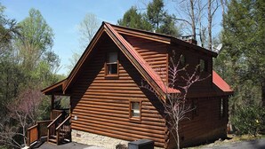 Una cabaña de troncos con base de piedra, escaleras de madera y techo rojo.