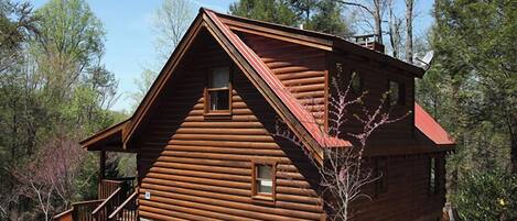 A log cabin with a stone foundation, a wooden staircase, and a red roof.